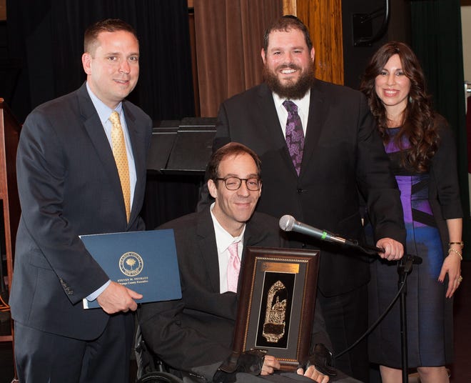 Eric Muhlrad, seated, is honored during an event prior to Passover hosted by Chabad of Orange County which is led by Rabbi Pesach and Chana Burston, standing right. Attending was Orange County Executive Steve Neuhaus, left, who presented a certificate. Photo by Aiken Studio