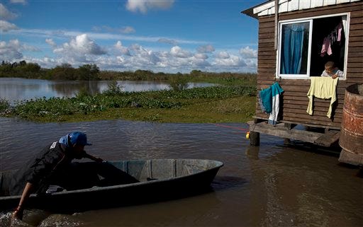 A man navigates a flooded road, outside a home in Villa Paranacito, Entre Rios, Argentina, Thursday, April 28, 2016. The Argentine Red Cross estimates more than 30,000 people have been affected by the flooding, with more than 2,000 evacuated after rain swelled rivers, swamping fields and towns nationwide. (AP Photo/Natacha Pisarenko)