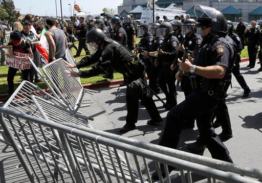 Police officers push down barricades used by a group protesting Republican presidential candidate Donald Trump outside of the Hyatt Regency hotel during the California Republican Party 2016 convention in Burlingame, Calif., Friday, April 29, 2016. (AP Photo/Eric Risberg)