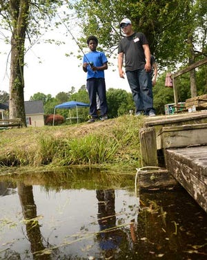 Amir Holmes, 10, fishes while volunteer Chris Allard watches during Tuesday’s Fisher of Kids Angler Academy in Snow Hill.