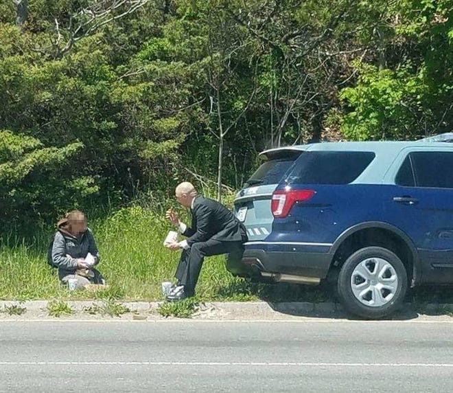 State Trooper Luke Bonin and a homeless woman off the side of a road in Fall River enjoy conversation and a lunch that Bonin bought after seeing the woman there, Wednesday, May 11. This photo went viral on Facebook today, after it was shared by the Massachusetts State Police.
