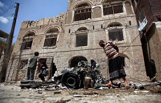 FILE - In this Tuesday, June 30, 2015 file photo, People stand amid wreckage of a vehicle at the site of a car bomb attack near a military hospital in Sanaa, Yemen. The World Health Organization says nearly 1,000 people have been killed worldwide in attacks on medical facilities in conflicts over the past two years in violation of humanitarian norms. (AP Photo/Hani Mohammed)