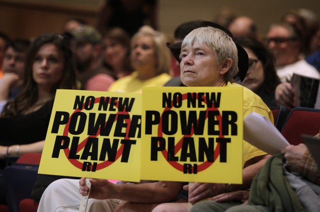 Betty Mencucci holds up twin signs stating her opinion of the Burrillville power plant at a public hearing Monday at Burrillville High School. The Providence Journal / Kris Craig
