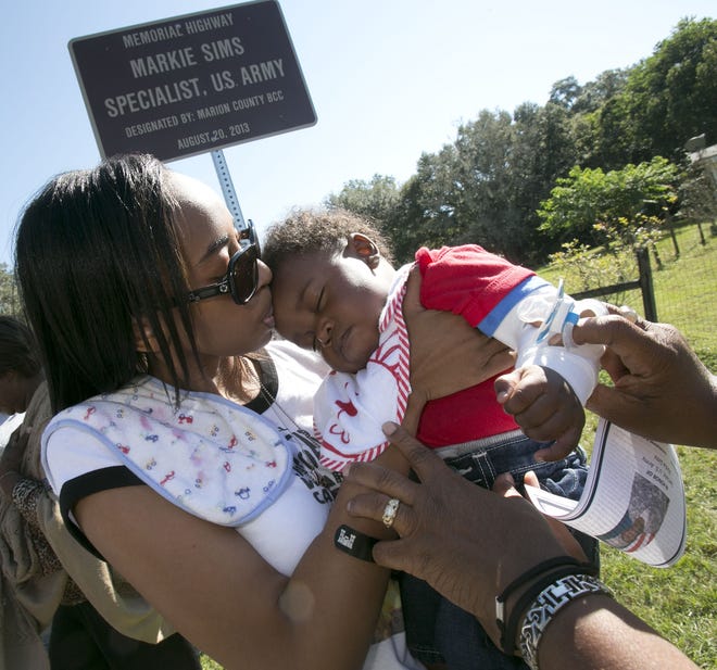 Shakelia Sims, left, gives her son Kayden Sims, 6-months-old, a kiss after Northwest 155th Street, in Reddick, FL, was dedicated to Markie Sims, Specialist with the U.S. Army, who was killed in Afghanistan on December 29, 2012. Markie was married to Shakelia and and she was pregnant when Sims was killed. Three different road dedications were held Friday morning, October 25, 2013, across Marion County. Army Specialist Fourth Class Clarence Williams III, Specialist Markie Sims and Fire Chief John "Junior" James, all had roads named in their honor. Both Williams and Sims were killed in action in 2012, while Chief James passed away May 22, 2012.