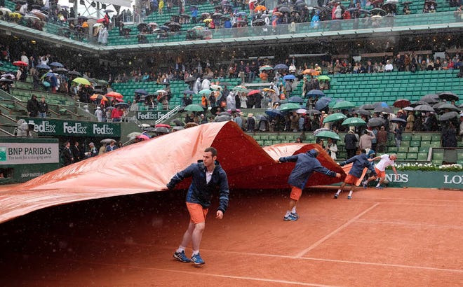 Alastair Grant Associated Press Workers cover the clay court at Roland Garros during a rain delay at the French Open on Monday. Matches halted by tournament's first rainout in 16 years were moved to today. The French Open is the only Grand Slam event without a roof.