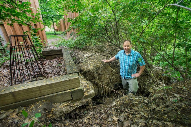 Shawn Miller stands in an eroded area outside his fenced yard on Kaitlin Court in East Peoria. Miller's property abuts property that suffered serious damage in a landslide three years ago and now watches the erosion expand as storm water runoff beneath and around the drain at left.