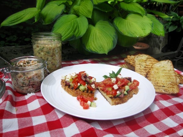 Grilled bread topped with a chopped Greek salad, plus other spreads in jars on the side: salmon rillettes, left, and a white bean salad