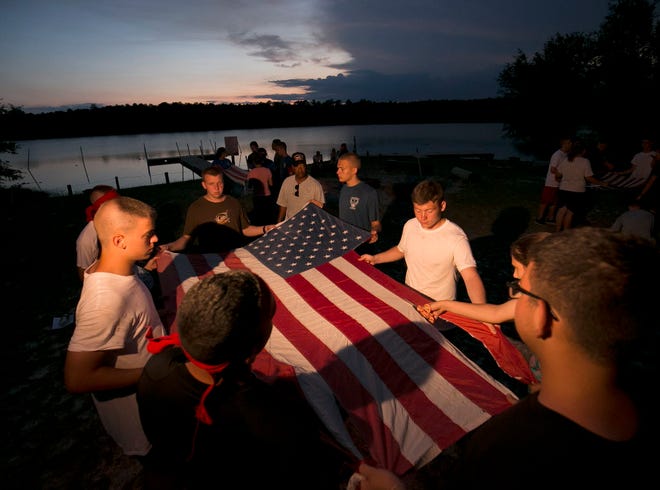 As the sun sets at Camp Sozo in the Ocala National Forest Thursday night, June 2, 2016, a cadet cuts off the third stripe of the American flag, representing one of the original 13 colonies, New Jersey, as total of 21 cadets and 7 senior staff from Belleview High School's Air Force JROTC, took part in a flag retirement ceremony. A total of 50 flags were retired Thursday night. The group spent the week in a summer leadership camp.