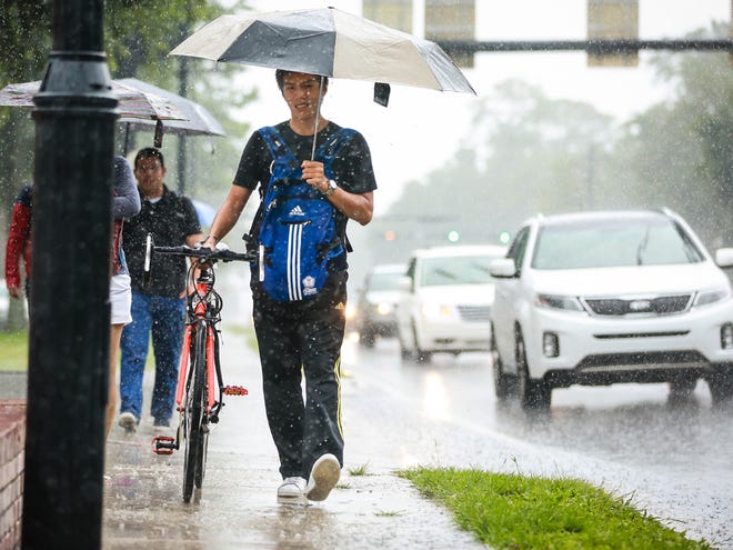 Umbrella-wielding pedestrians make their way near University Avenue and 13th Street as a band from Tropical Storm Colin brings heavy rainfall on Monday.