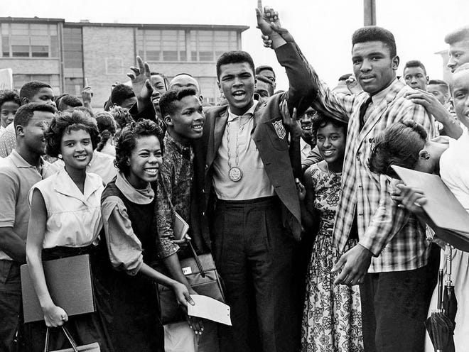 In this Sept. 10, 1960, file photo, cheering students of Central High School surround Olympic boxing champion Cassius Clay, raising hand in center, and wearing Olympic medal, in Louisville, Ky. Boxing great Cassius Clay's hometown newspaper, The Courier-Journal, refused to call him Muhammad Ali for years after he adopted the Muslim faith and changed his name. Louisville's daily paper has apologized 50 years later for continuing to refer to him as Cassius Clay for years after he converted in 1964. It did not consistently refer to him as Muhammad Ali until 1970.