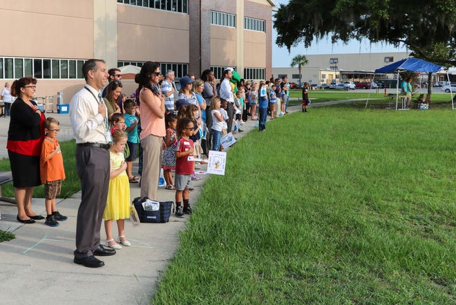 Children and parents, from Naval Facilities Engineering Command Southeast, stand at attention on June 9 as they paid respect during raising the flag and playing the national anthem at the salute of morning colors. The group was outside preparing for the command's annual Bring Your Kids To Work Day event.