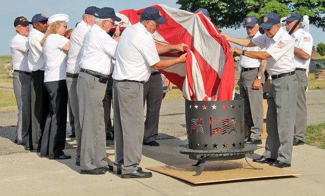Members of the Jonesville American Legion Post 195 ceremoniously lower a large American Flag into a burn pit Tuesday evening at the beginning of the ceremony at Freedom Memorial. COREY MURRAY PHOTO