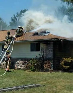 Firefighters work to ventilate a roof and extinguish flames Sunday afternoon. COURTESY PHOTO