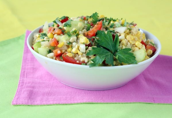 A grain salad made with fresh summer vegetables, including corn and diced onion, cucumber and red bell pepper.