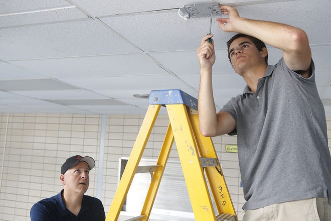 Velocity Solutions contractor Jim Lass, left, watches as Matt Violet, who graduated with Middletown High School’s class of 2015, installs new wireless access points in the MHS school cafeteria on Wednesday.
