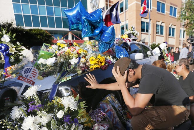 Vicente Alfaro, 15, of Irving, Texas, kneels and places his hand on a Dallas police cruiser after leaving a bundle of flowers at a makeshift memorial outside of Dallas Police Department headquarters, Friday, July 8, 2016, in Dallas. Alfaro, a student at Jack E. Singley Academy in Irving, is part of the Dallas Police Explorers. (AP Photo/Tony Gutierrez)