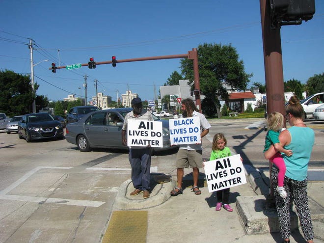 jared.keever@staugustine.com Erica Kiernan pauses to snap a picture of her daughter as she poses with local activist James Jackson and Michael McDermott during a Friday evening demostration on the corner of King Street and U.S. 1.