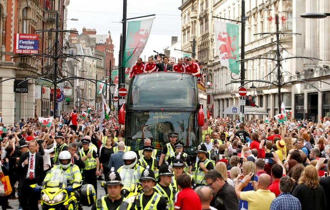 Wales soccer players ride atop an open top bus, with front left to right, Ashley Williams, Gareth Bale, manager Chris Coleman, acknowledge the crowd of fans during their homecoming in Cardiff City centre, Wales, Friday July 8, 2016. Wales return home to a hero's welcome after unexpectedly reaching the semi-finals of the Euro 2016 soccer championships knocked out by Portugal. (Paul Harding / PA via AP)