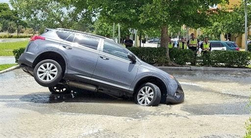 A vehicle was partially swallowed by a 10-foot-by-10-foot sinkhole on Thursday in Cooper City, Fla. Dolores Otero drove toward the drive-thru and her car went nose-first into the water. One of the car's back tires was left hanging in the air. Otero and her grandson got safely out of the vehicle, which began to fill with water.