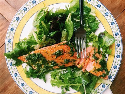 This May 13, 2016 photos a fillet of salmon smothered in an herb marinade served over a tender green salad, in New Milford, Conn. This warm-weather recipe combines salmon bathed in olive oil and herbs with spring-y greens and salad. It’s the kind of lighter, brighter meal we tend to want during summer. (AP Photo/Katie Workman)