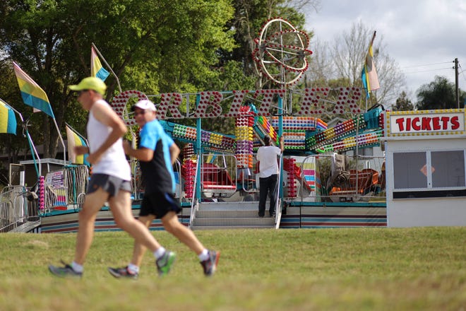 Runners jog past a ride being set up in preparation for Pig on the Pond at Clermont Waterfront Park in Clermont on March 11, 2015. (Daily Commercial/file)