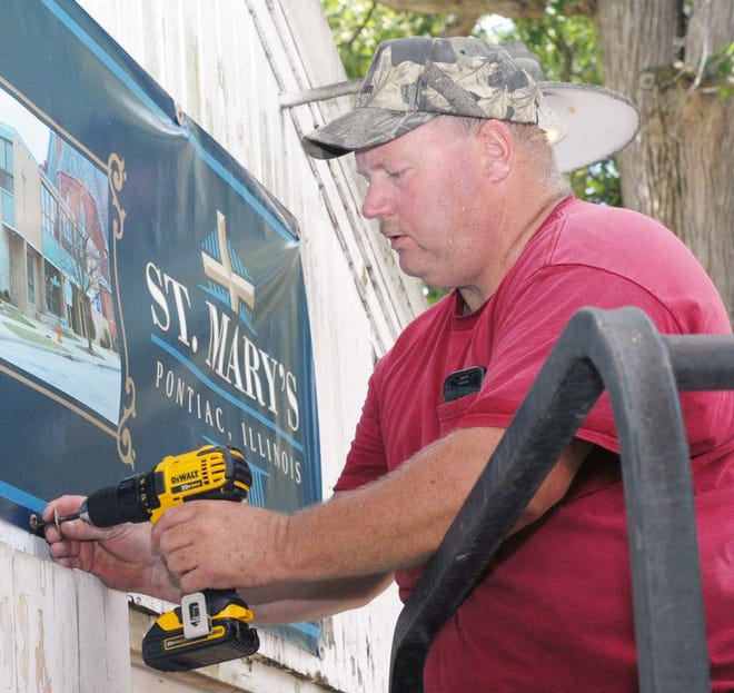 Mark Corrigan, co-organizer of the St. Mary’s fair kitchen at the Livingston County Ag Fair and 4-H Show, drills in the screws holding up the St. Mary’s sign on Tuesday.