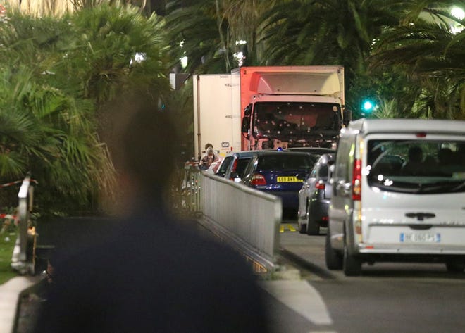 A policeman stands, watching the truck used for the attack near the scene of an attack after a truck drove onto the sidewalk late Thursday, and plowed through a crowd of revelers who gathered to watch the fireworks in the French resort city of Nice, southern France, Friday, July 15, 2016.