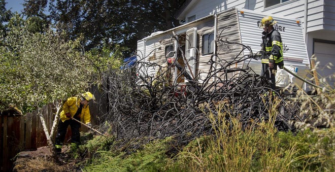 Firefighters mop up a small blaze in an arborvitae near 3750 Emerald Street in South Eugene. A camping trailer was scorched in the blaze that was extinguished quickly with the help of fast-acting neighbors. (Andy Nelson/The Register-Guard)