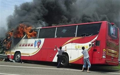 In this photo provided by Yan Cheng, a policeman and another man try to break the windows of a burning tour bus on the side of a highway in Taoyuan, Taiwan, Tuesday, July 19, 2016. The tour bus carrying visitors from China burst into flames on a busy highway near Taiwan's capital on Tuesday, burning to death over 20 people on board, officials said .(Yan Cheng/Scoop Commune via AP)