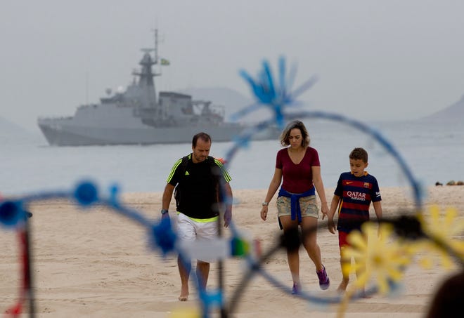 A family walks on the shore of Copacabana beach backdropped by a Brazilian navy vessel, in Rio de Janeiro, Brazil, Thursday, July 21, 2016. Brazilian police arrested 10 people who allegedly pledged allegiance to the Islamic State group on social media and discussed possible attacks during the Rio de Janeiro Olympics, officials said Thursday. (AP Photo/Silvia Izquierdo)