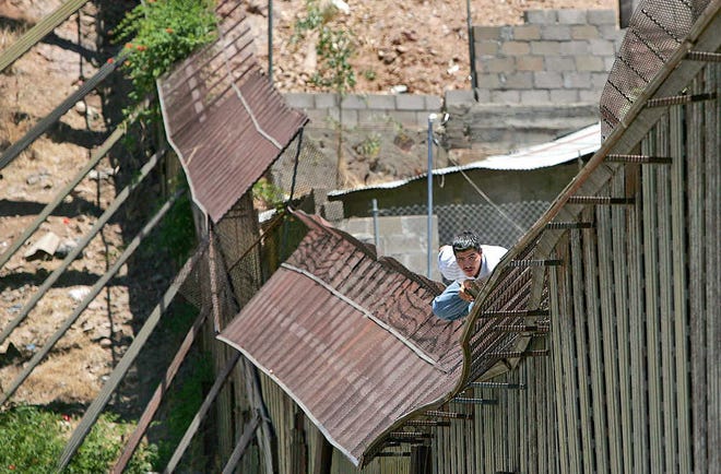 FILE - In this May 31, 2006, file photo, a man climbs over the international border into Nogales, Ariz., from Nogales, Mexico. Presumptive GOP nominee Donald Trump's push for a border wall is not a new idea, and since World War I, has been pursued often. Historians said opponents of Mexican immigration have advocated for a wall off and on for about 100 years with little results due to changing technologies and pressure to divert enforcement attention elsewhere. (AP Photo/Matt York, File)