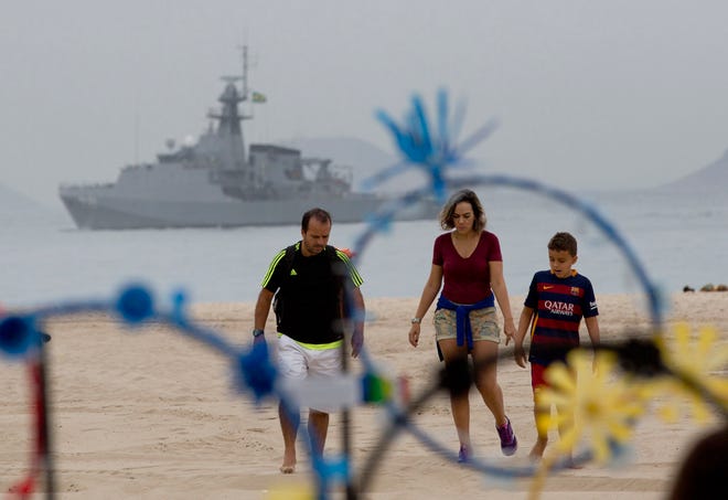 A family walks on the shore of Copacabana beach backdropped by a Brazilian navy vessel, in Rio de Janeiro, Brazil, Thursday, July 21, 2016. Brazilian police arrested 10 people who allegedly pledged allegiance to the Islamic State group on social media and discussed possible attacks during the Rio de Janeiro Olympics, officials said Thursday.