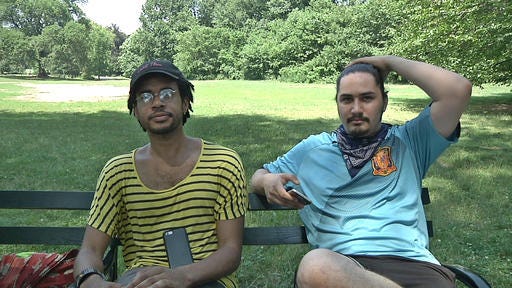 In this July 13, 2016, frame grab from video, Jordan Clark, left, and Lewis Gutierrez sit in Prospect Park as they talk about their new "Pokemon Go" business in the Brooklyn borough of New York. (AP Photo/Ezra Kaplan)