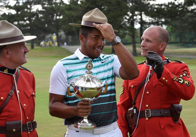 Jhonattan Vegas, of Venezuela, holds the trophy as he adjusts a Stetson borrowed from a Mountie, after his victory in the Canadian Open golf tournament, Sunday, July 24, 2016, in Oakville, Ontario.