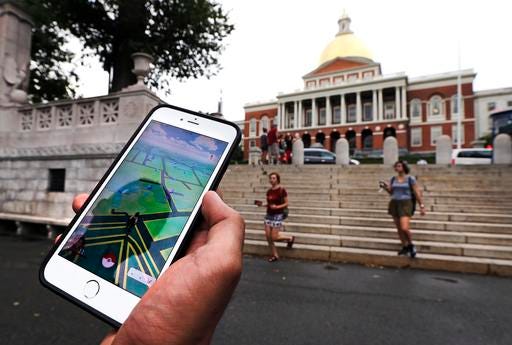 In this Monday, July 18, 2016, photo, a "Pokemon Go" player shows his mobile phone while walking through the Boston Common, outside the Massachusetts Statehouse in Boston. Historical markers dot the landscape of old cities, barely noticed by passers-by. The founder of the volunteer-based historical markers website that licensed its data to game-maker Niantic Labs five years ago said he hopes enough people take their eyes off the Pokemon they’re trying to catch to read the history on the markers. On the opposite side of the wall, left, is a bronze memorial to Robert Gould Shaw and the 54th Regiment Massachusetts Volunteer Infantry, comprised of black Union soldiers who fought in the Civil War. (AP Photo/Charles Krupa)