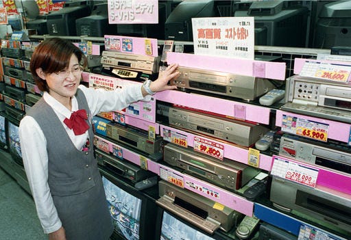 In this 1998 photo, a salesclerk shows VHS video casette recorders at a home and electrical appliance store in Osaka. Japanese electronics maker Funai Electric Co. says it's yanking the plug on the world's last video cassette recorder.