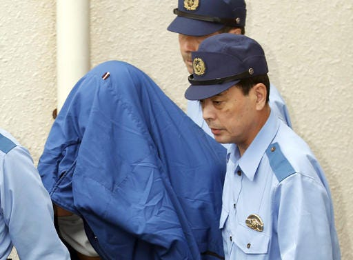 Satoshi Uematsu, left, the suspect of Tuesday's knife attack at a home for the mentally disabled, is escorted as he leaves a police station in Sagamihara, outside Tokyo to be sent to prosecutors Wednesday, July 27, 2016. The deadliest mass killing in Japan in the post-World War II era raised questions about whether Japan's reputation as one of the safest countries in the world is creating a false sense of security. (Yohei Kanasashi/Kyodo News via AP)