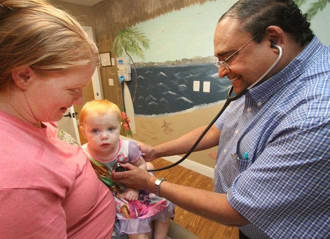 Dr. Peter DeSouza, at right, starts his examination of 15 month old Addison Zook, being held by mom Cassidee Zook, at the Family Health Source clinic in DeLand. The federally-funded clinic offering primary care is similar to one proposed for Daytona Beach. News-Journal/David Tucker