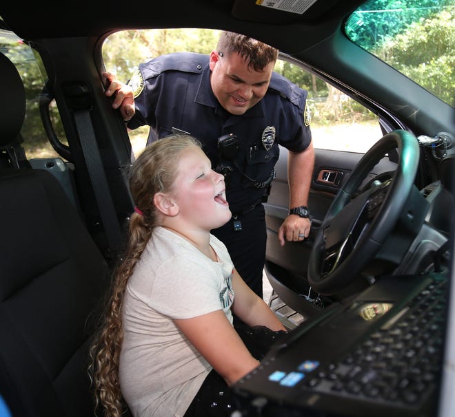 Grace Trafford, 6, a Daisy in Girl Scout Troop 3920 in Belleview, laughs as she got to make the siren wail while getting a tour of a police patrol car from officer Mikey Miley of the Belleview Police Department in Belleview, Fla. on Wednesday, July 27, 2016. Grace wanted to make something to help law enforcement feel special and came up with the idea of giving bracelets to them to show support for law enforcement. She made a several of them and took them to the Belleview Police Department on Tuesday. On Wednesday, Grace got a tour of the police department and had the opportunity to meet officers and get a tour of a police car. (Star-Banner Photo/Bruce Ackerman) 2016.
