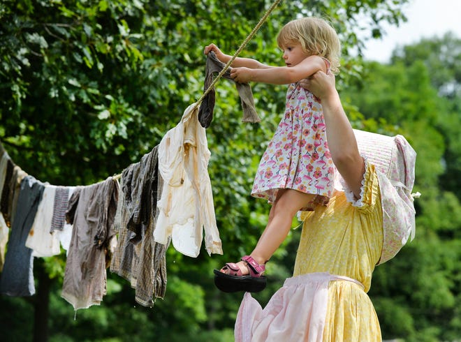 RON JOHNSON/JOURNAL STAR Three-year old Isabel Runge of Edwards gets a lift from re-enactor Kristi Smith to help hanging the laundry up to dry during a demonstration of life of rural Peorians in the mid 19th century during Pioneer Days at Sommer Park on Sunday.
