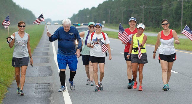 Ernest Albus, 92, waves a flag as he and six women runners trot along U.S. 82 east of Nahunta as he closes in on the Aug. 20 finish of his run from San Diego to St. Simons Island.
