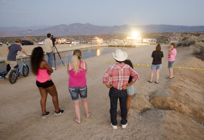 Neighbors and onlookers watch San Bernardino County Fire Department and other agencies recover a body from the California Aqueduct near Halinor Street on Monday night. (James Quigg, Daily Press)