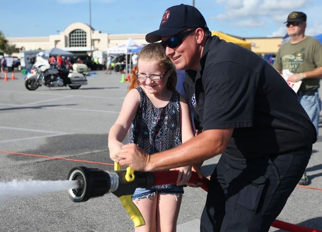 Amanda Depriest, 8, aims a fire hose at a wooden target Tuesday with help from Lynn Haven Senior Firefighter Bobby Mayo. The Panama City Police Department and Naval Support Activity Panama City Security Department sponsored the ninth annual National Night Out on Tuesday in the parking lot of Panama City Mall.