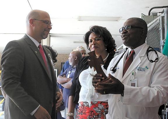 Dr. Eugene Nwosu, at right, receives a wooden cross from Adam Walker, left, as Nwosu's wife, Mary, looks on Thursday morning at Candler Hospital. Nwosu, a local cardiologist, is retiring to expand a clinic and start a cardiology program in his native Nigeria this fall, and St. Joseph's/Candler is donating more than $100,000 of supplies to aid him. (Dash Coleman/Savannah Morning News)
