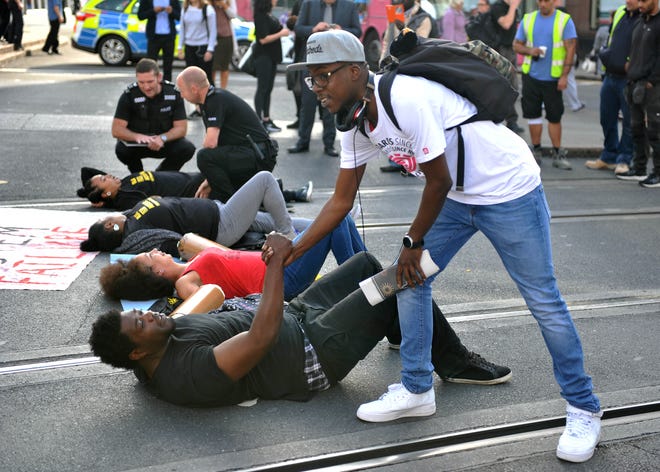 A man shakes hands with one of the activists as they lay on the road outside Nottingham Theatre Royal during an attempt to shut down part of the city centre tram and bus network in Nottingham, England Friday Aug. 5, 2016 to protest for social justice movement Black Lives Matter. Activists affiliated with the U.S.-based group Black Lives Matter have blocked a road leading to Heathrow Airport, and Nottinghamand city centre along with protests in other British cities (Edward Smith/PA via AP)