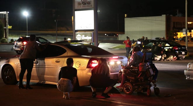 Protesters hide behind cars after shots were fired Tuesday, Aug. 9, 2016, in Ferguson, Mo., during a demonstration on the second anniversary of Michael Brown's death. Witnesses told an Associated Press reporter that a car sped through a group of protesters who were blocking a street during the demonstration marking two years since the unarmed black 18-year-old's fatal shooting by a white police officer. They said the car struck a young man so hard that he flew into the air. As the car drove away, shots were fired, they said. (Robert Cohen/St. Louis Post-Dispatch via AP)