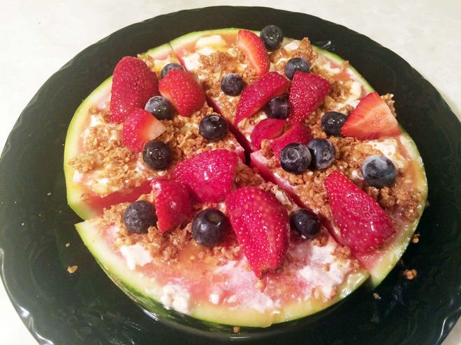 Watermelon pizza is a watermelon topped with softened cream cheese, granola and fruit.