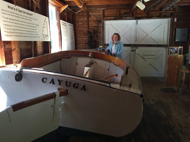 Osterville Historical Museum Director Jennifer Williams in the museum's boat shed with the 1922 catboat Cayuga, one of 15 wooden boats on display here. PHOTO BY DEBI BOUCHER STETSON