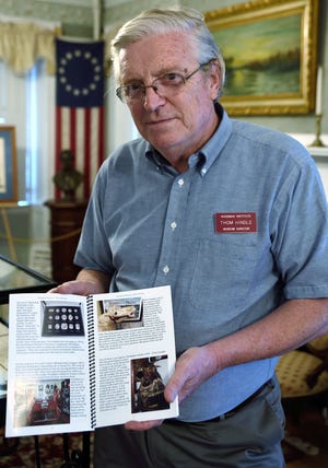 Thom Hindle holds a copy of a book featuring 100 unique items on display at the Woodman Museum to celebrate their 100th anniversary. Photo by John Huff/Fosters.com