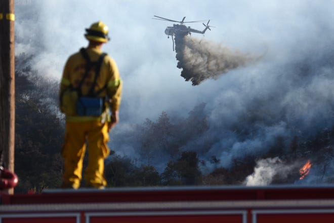 A San Bernardino County Fire Department firefighter watches a Helitanker make a water drop on the Bluecut Fire from Cajon Boulevard in Devore Thursday. After battling the 35,000-plus-acre blaze for a third day, officials announced that containment had grown to 22 percent. David Pardo, Daily Press